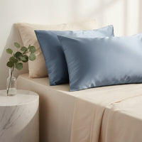 Slate blue mulberry silk pillowcases on a bed with cream linen, marble side table and eucalyptus