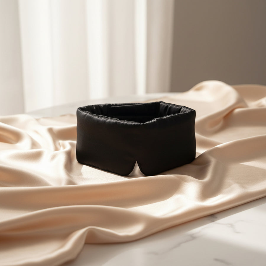 Black mulberry silk sleep mask resting on champagne silk fabric over white marble